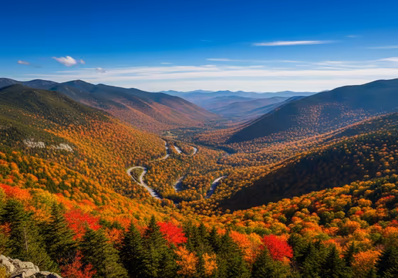 A scenic overlook on the Kancamagus Highway in autumn, showing a valley filled with vibrant red, orange, and yellow foliage.