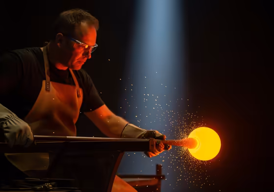 A master glassblower shaping a piece of molten glass during a live demonstration at the Corning Museum of Glass.