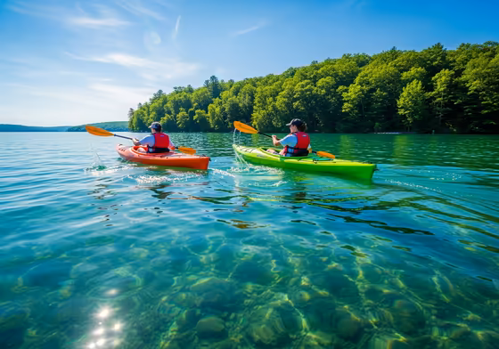Two people in colorful kayaks paddling on the calm, clear blue water of Skaneateles Lake on a sunny day.